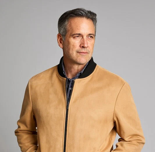 Man wearing a tan bomber jacket with black accents on a gray background